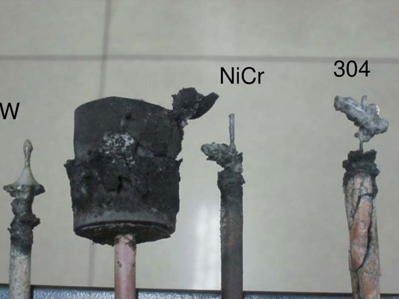 A visual comparison of anode materials after use, displaying the condition of Tungsten (W), Nichrome (NiCr), and 304 stainless steel, each exhibiting significant corrosion and degradation.